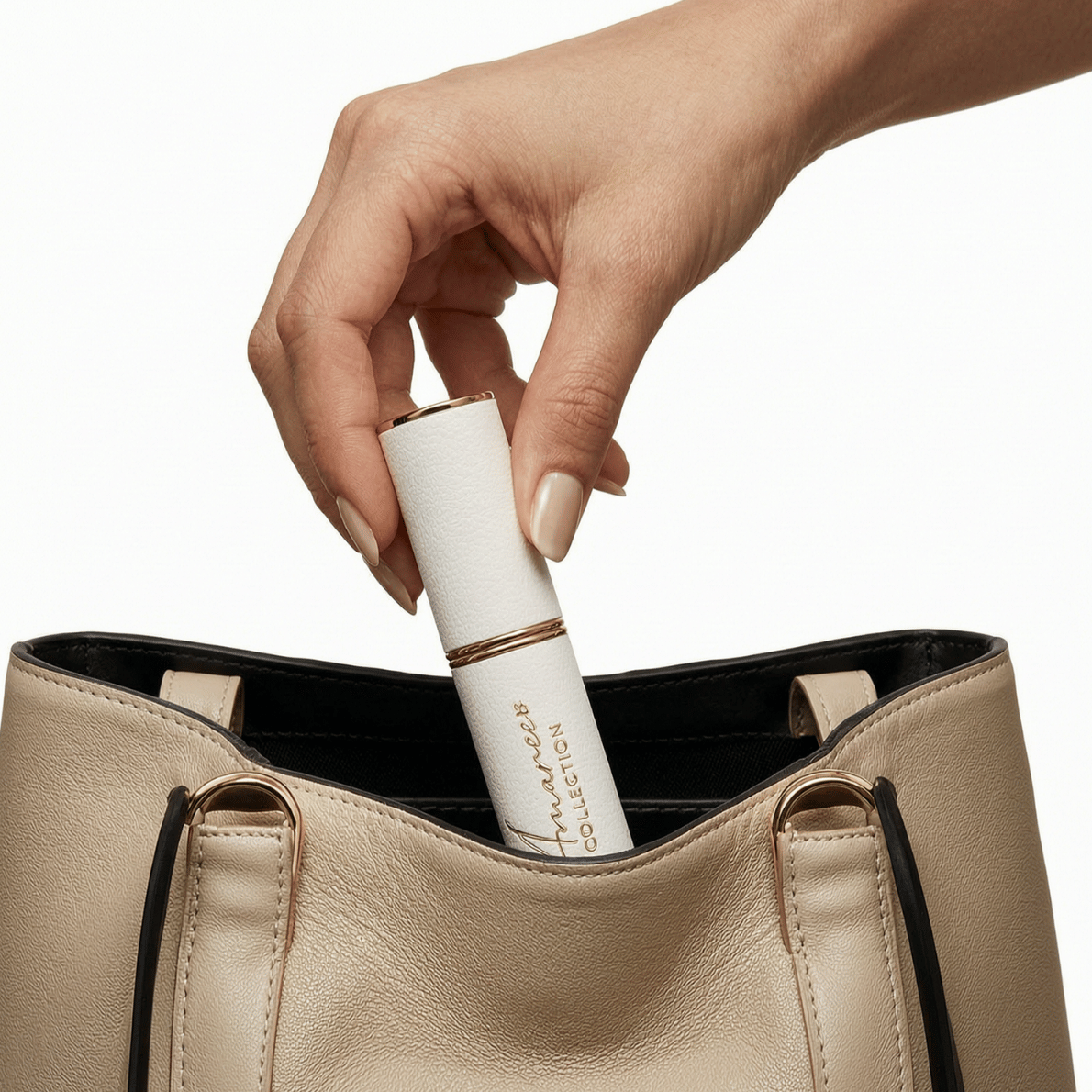 A hand with beige manicured nails reaches into a light beige leather tote bag and pulls out a slim white cylindrical cosmetic tube with gold trim and black text reading &