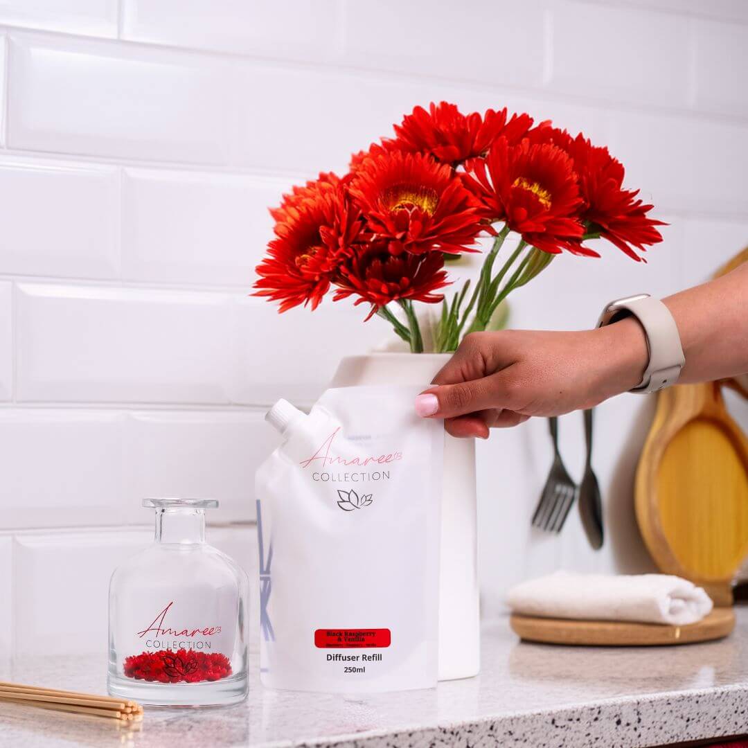 black raspberry vanilla reed diffuser refill 250ml beside red flowers on a white kitchen counter