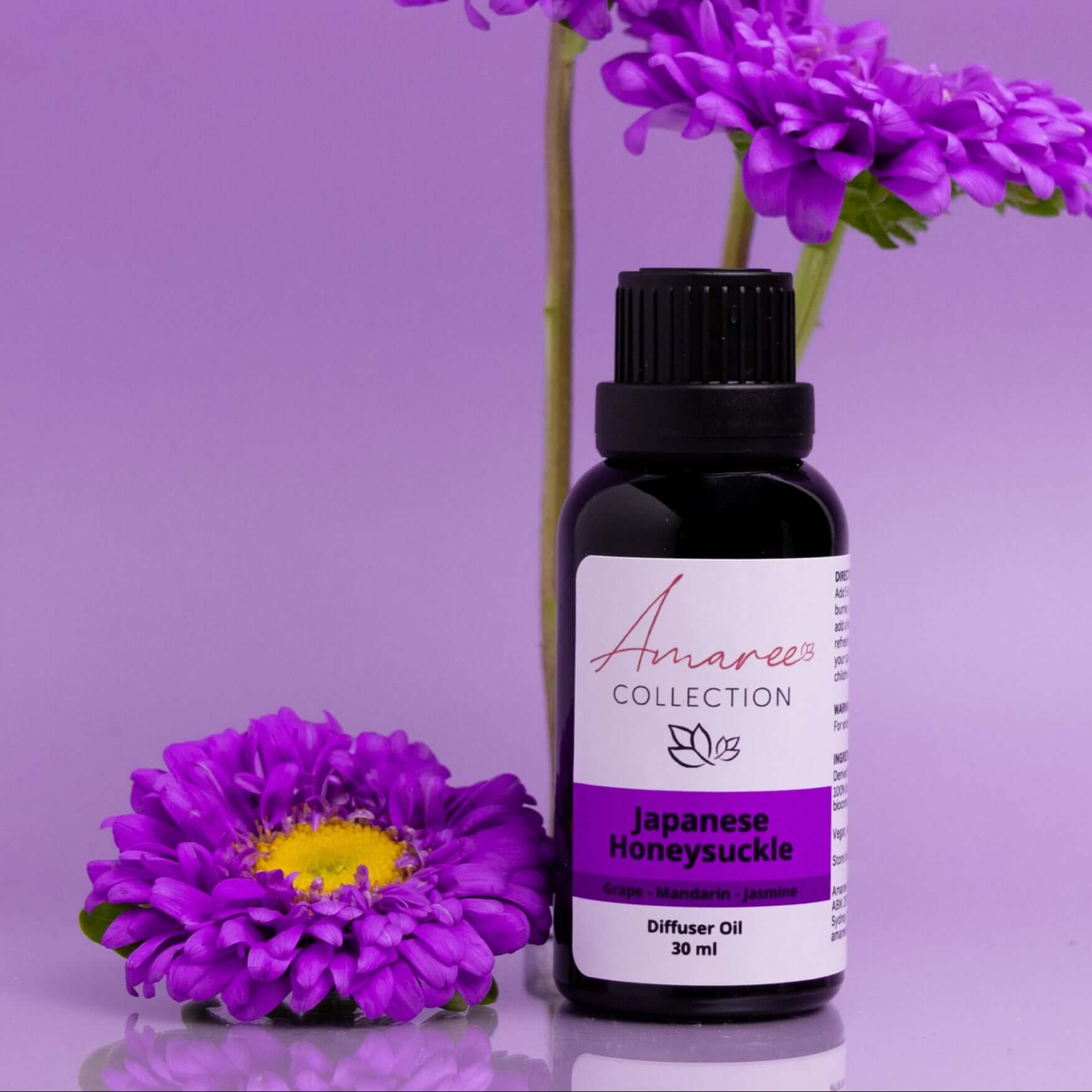 Japanese Honeysuckle Diffuser Oil bottle next to purple flowers on a pastel background.
