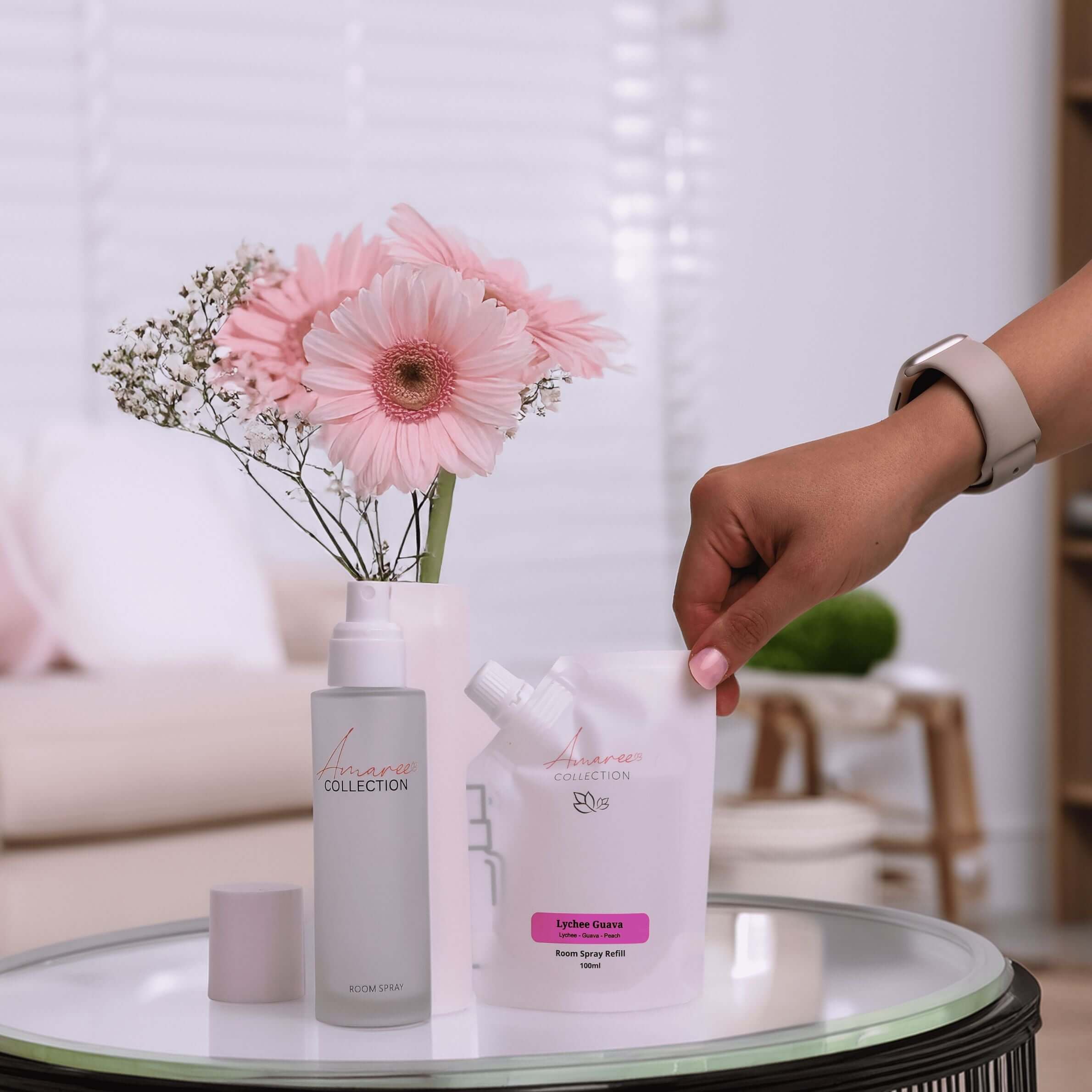 Lychee Guava Room Spray Refill 100ml eco-friendly pouches beside floral arrangement on a stylish table.