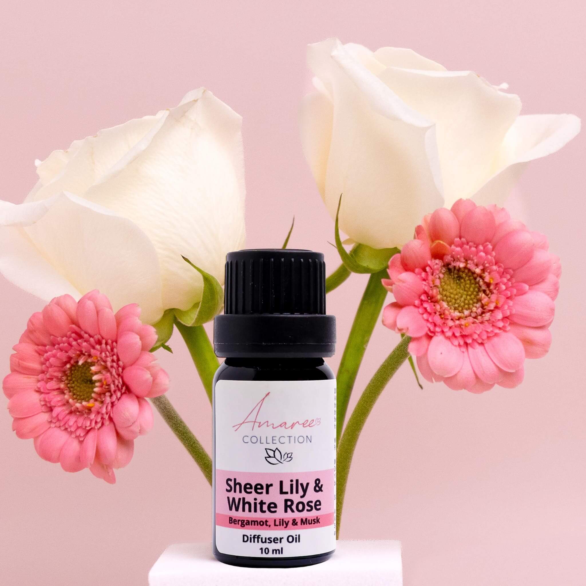 Sheer Lily & White Rose Diffuser Oil bottle surrounded by soft white and pink flowers on a pastel background.