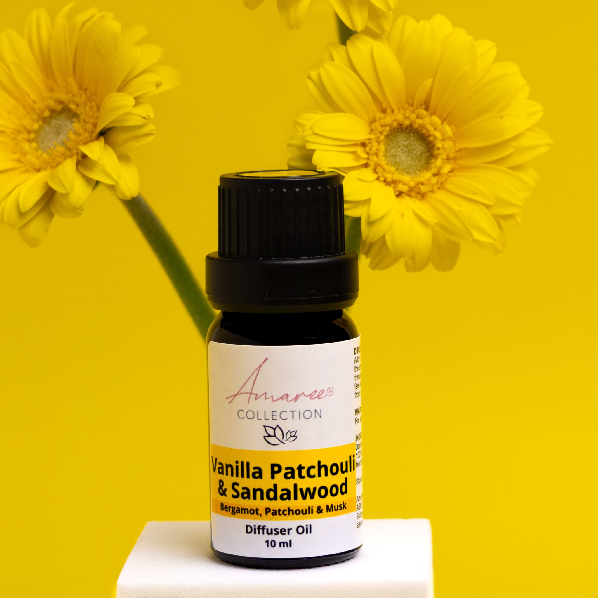 Vanilla Patchouli & Sandalwood diffuser oil bottle with yellow flowers on a yellow background