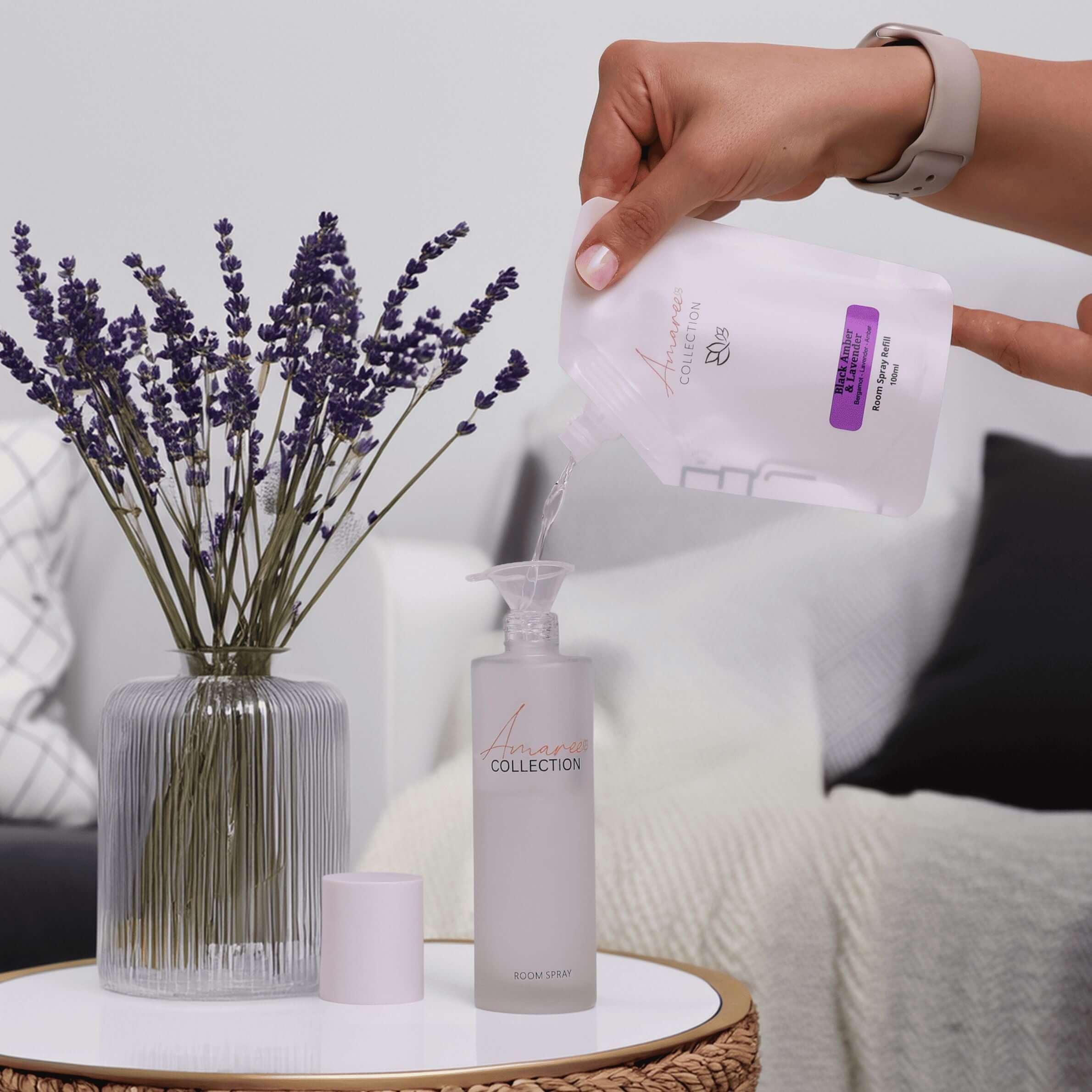 Black Amber & Lavender Room Spray Refill 100ml being poured into a spray bottle near lavender flowers.
