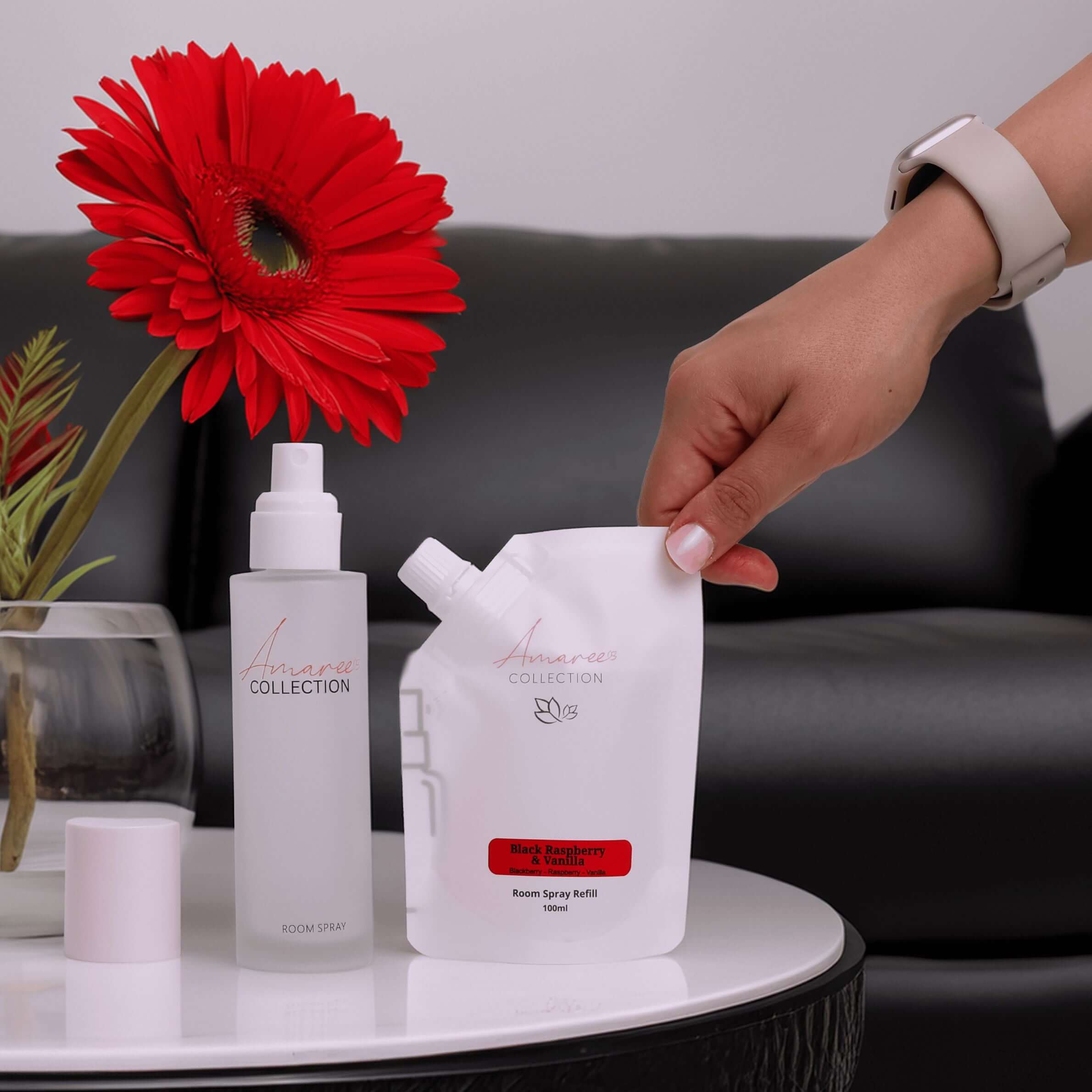 Black Raspberry & Vanilla Room Spray Refill 100ml displayed alongside a flower and room spray bottle on a table.