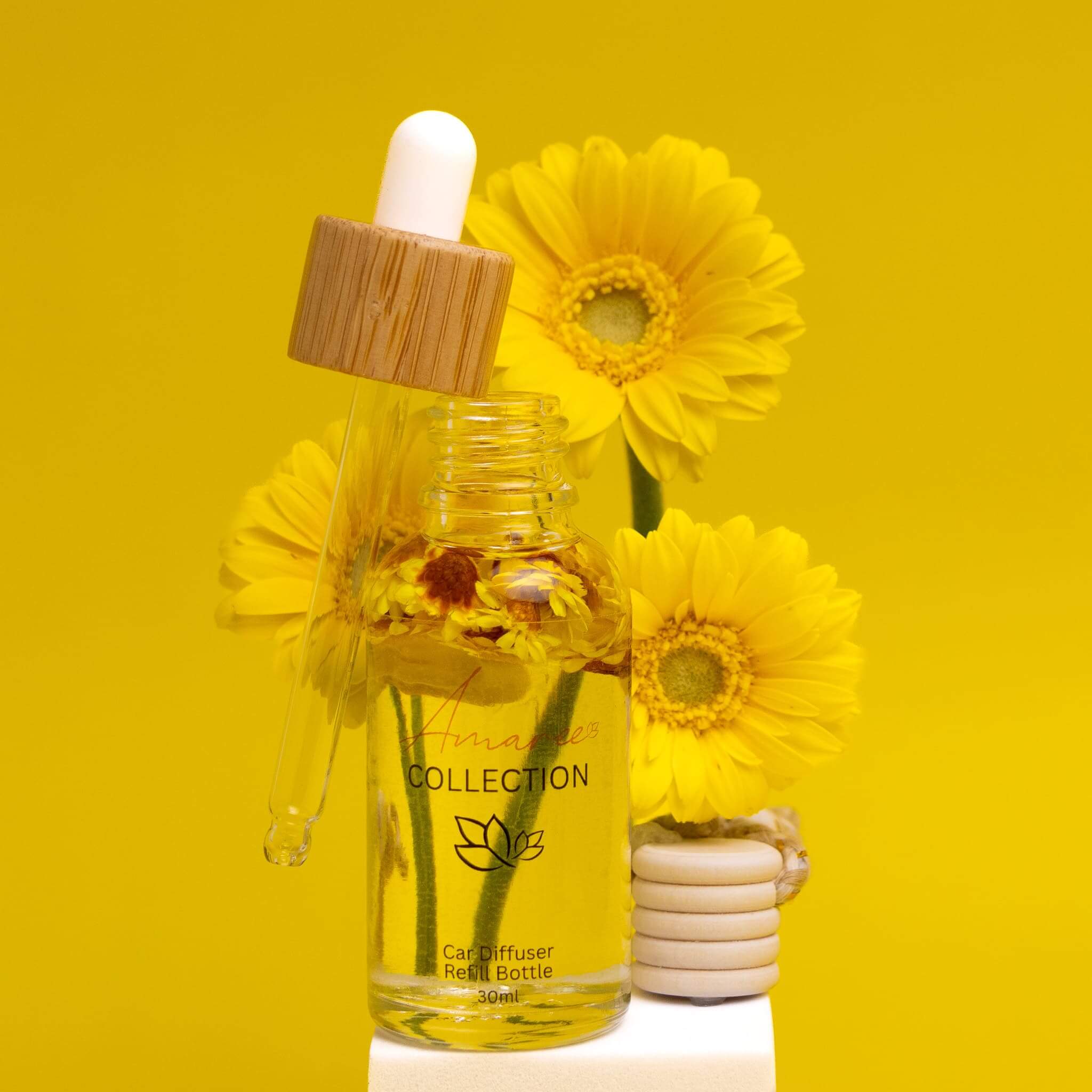 Vanilla Patchouli & Sandalwood Car Diffuser Refill bottle with dropper and yellow flowers on bright yellow background