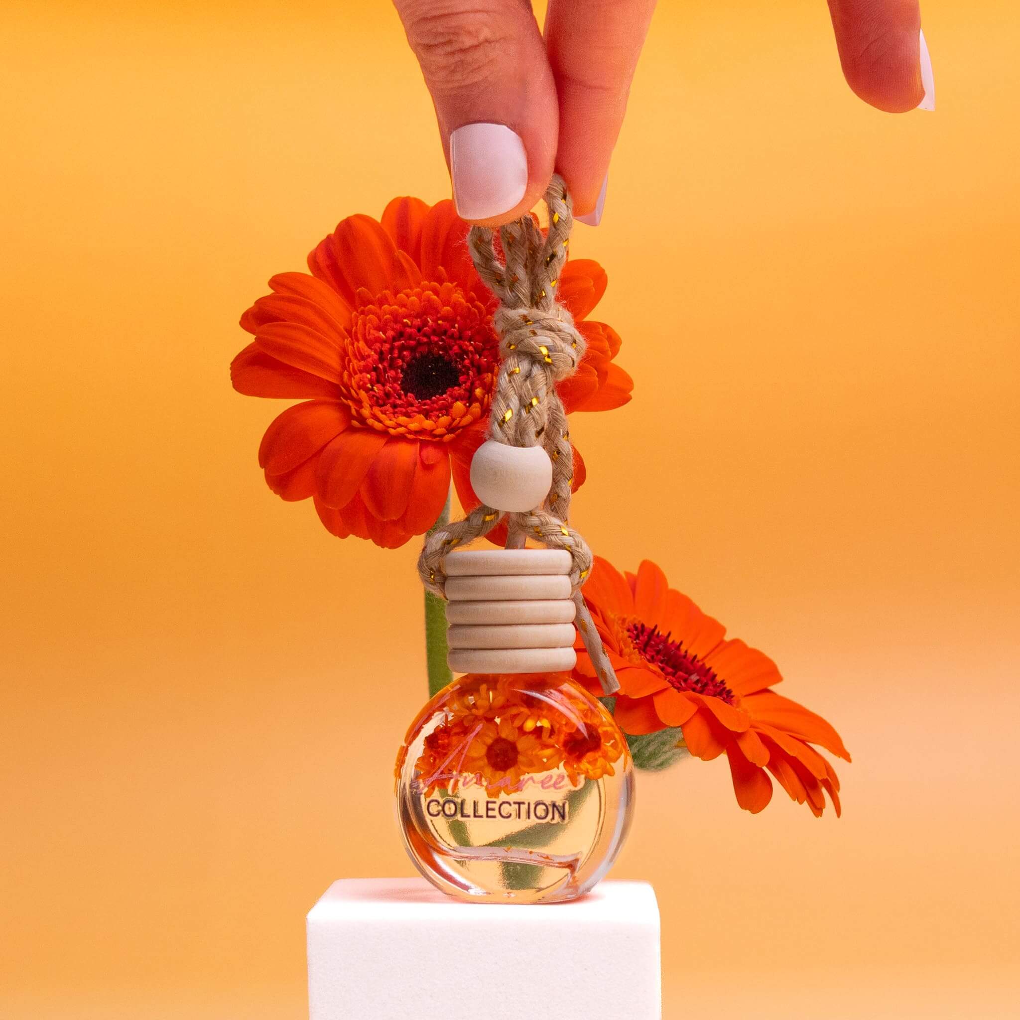 Cucumber & Melon Car Diffuser hanging bottle with bright orange flowers against an orange background