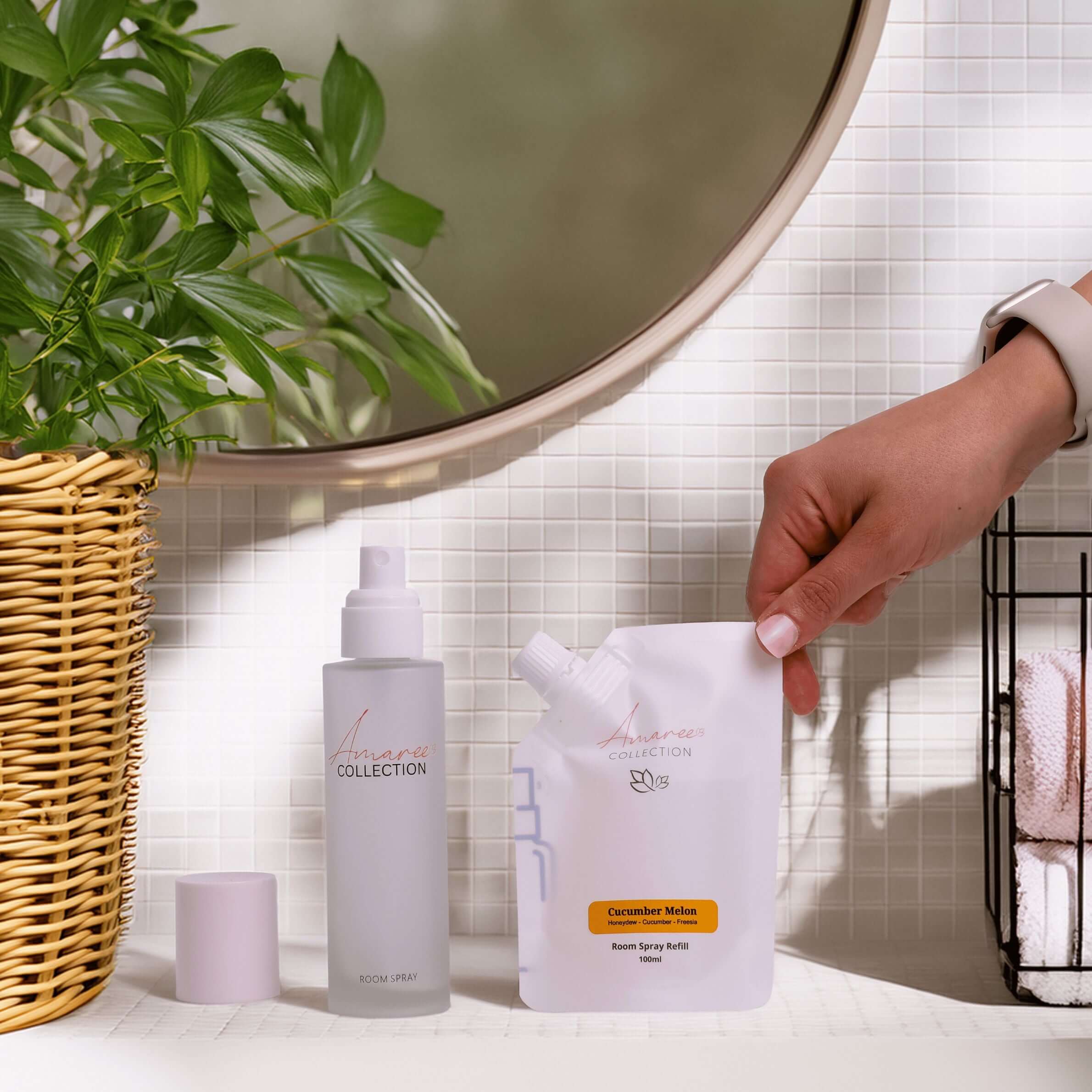 Cucumber Melon Room Spray Refill 100ml and spray bottle on a bathroom counter with plants.