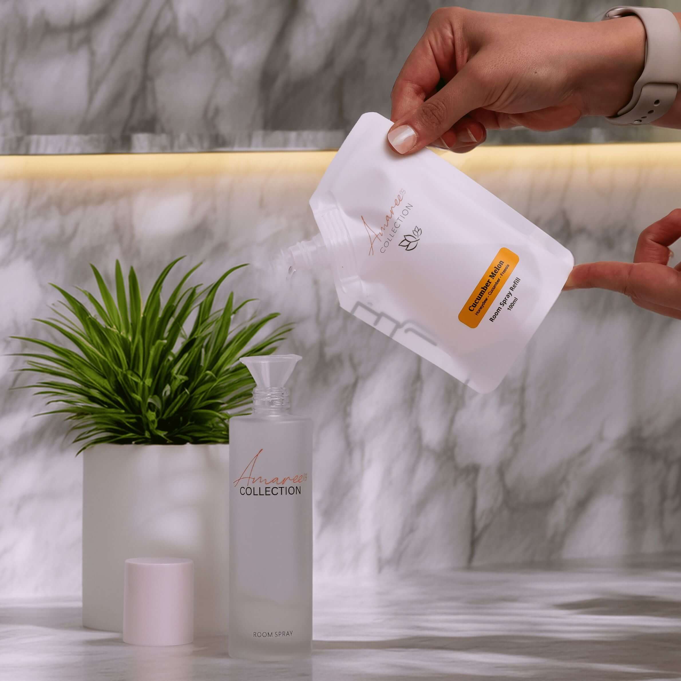 Cucumber Melon Room Spray Refill 100ml being poured into a bottle with greenery in the background.