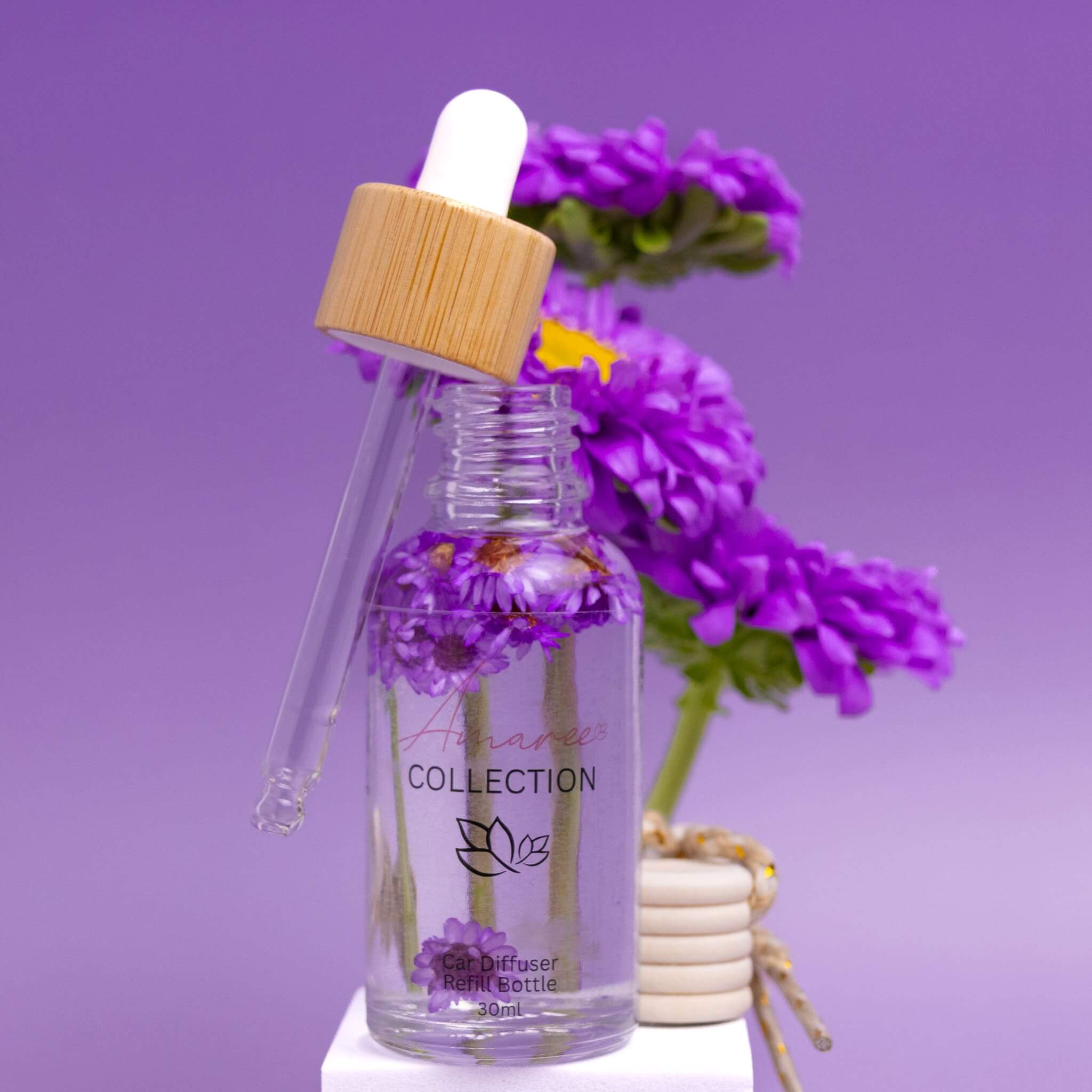 Japanese Honeysuckle Car Diffuser Refill glass bottle with dropper and purple flowers on purple background
