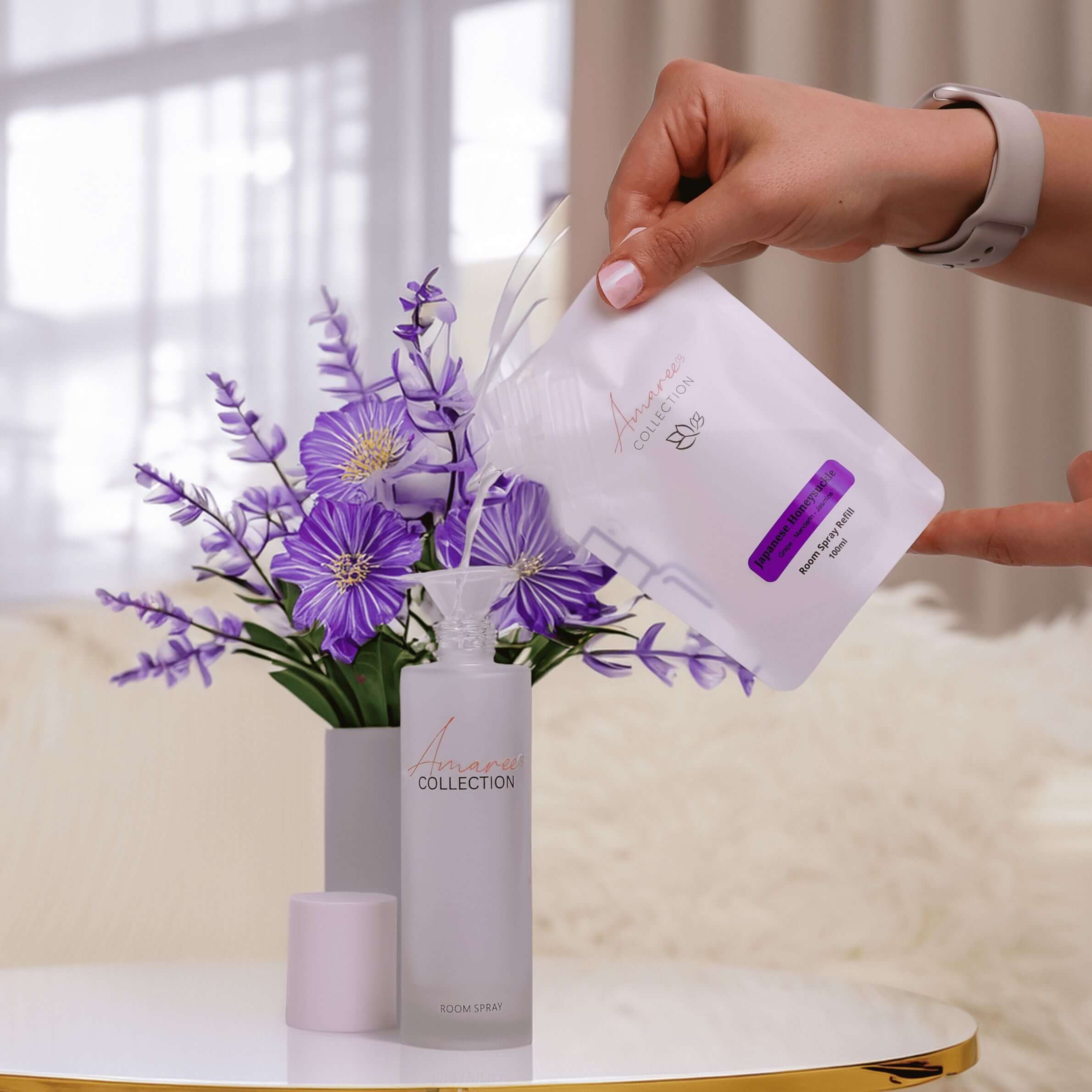 Japanese Honeysuckle Room Spray Refill 100ml being added to a floral room spray bottle with flowers in the background.
