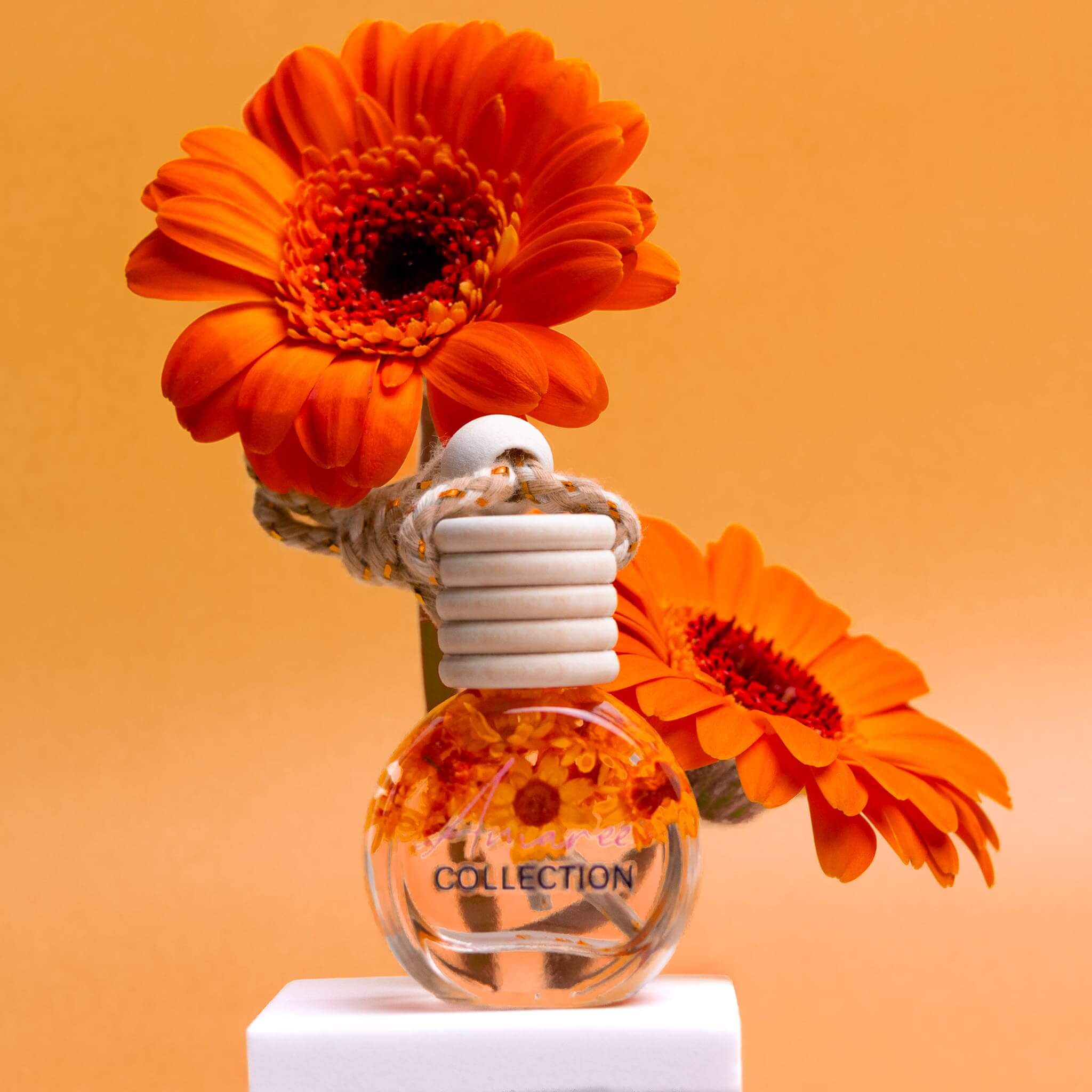 Lime, Basil & Mandarin Car Diffuser glass bottle with bright orange flowers on orange background