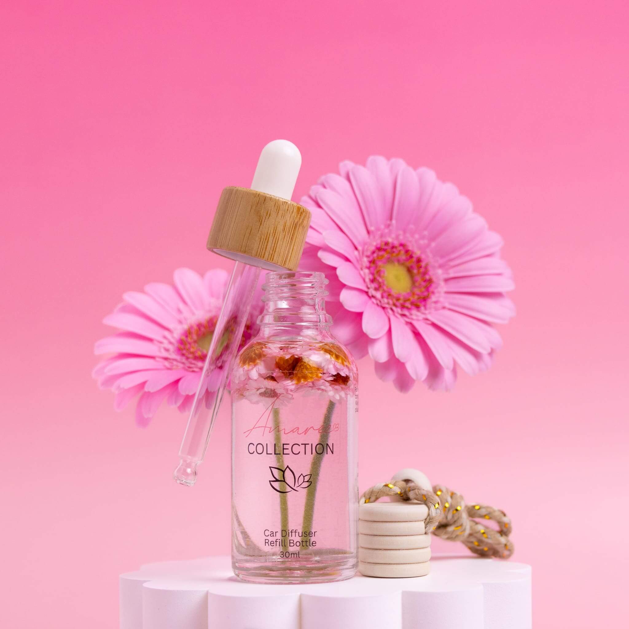Lychee Guava Car Diffuser Refill bottle with dropper and pink flowers on pedestal against bright pink background