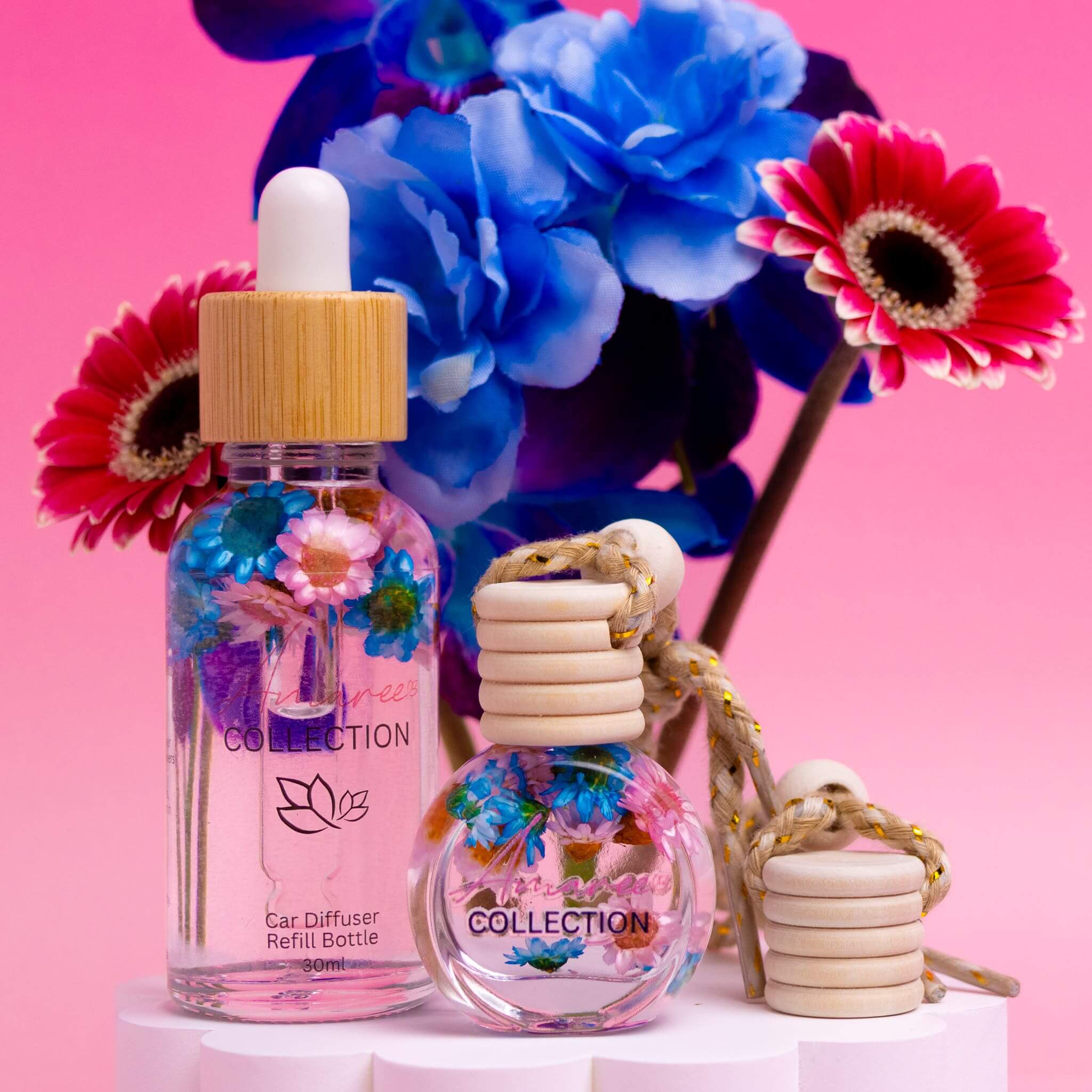 Pink Champagne & Exotic Fruits Car Diffuser Kit with colorful flowers and refill bottle on pink background.