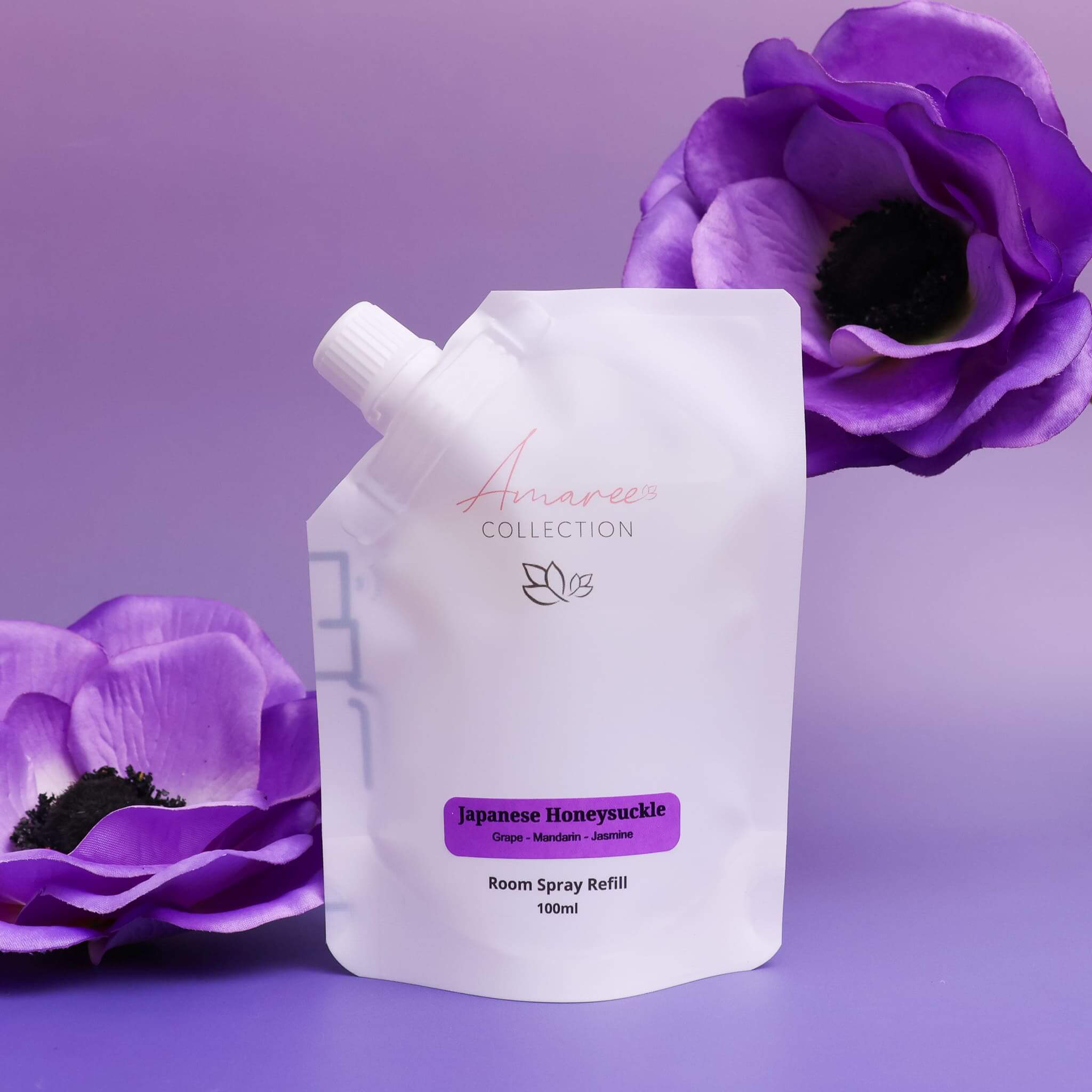 Japanese Honeysuckle Room Spray Refill 100ml in a sleek pouch with purple flowers in the background.