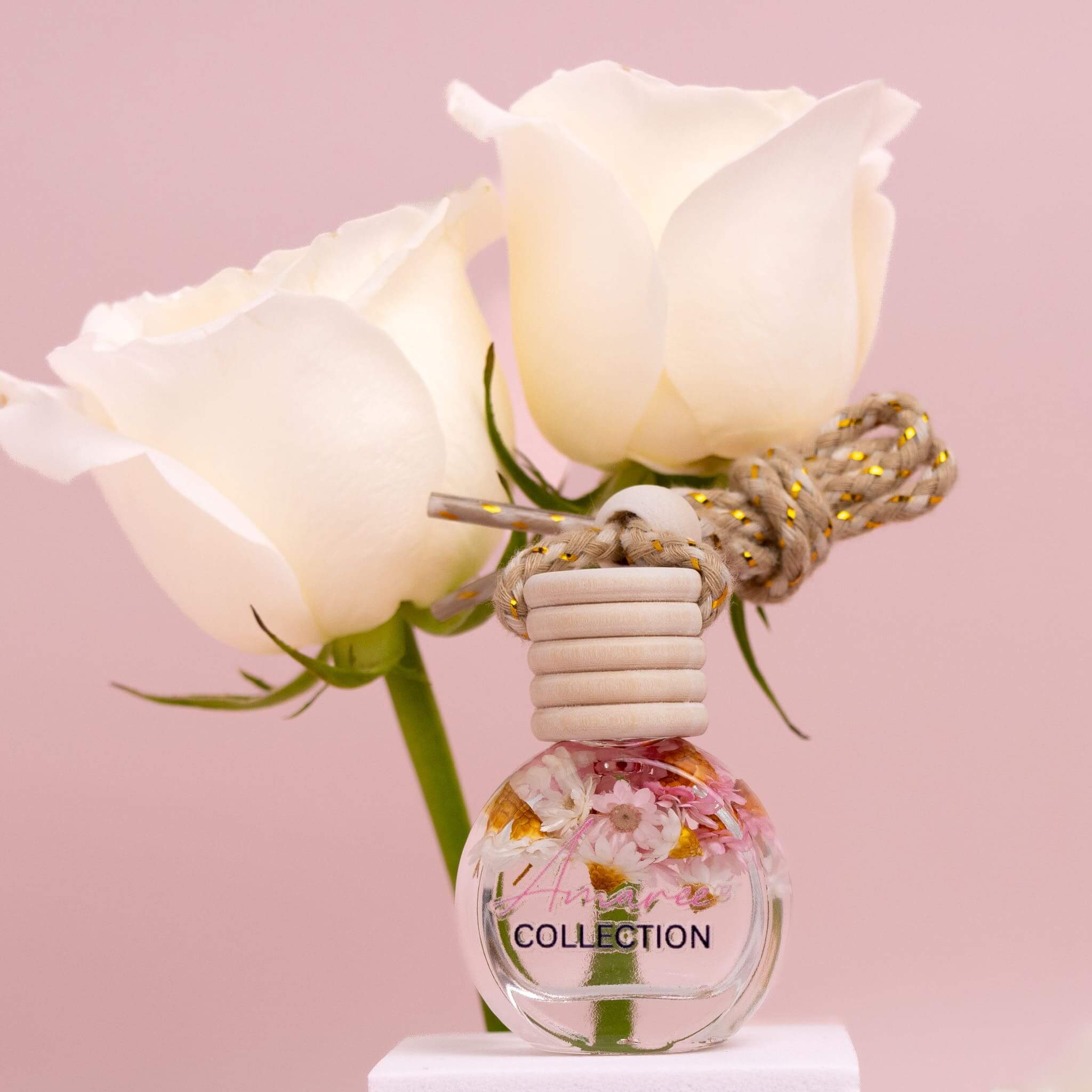 Sheer Lily & White Rose Car Diffuser with soft floral fragrance bottle against white roses on pink background