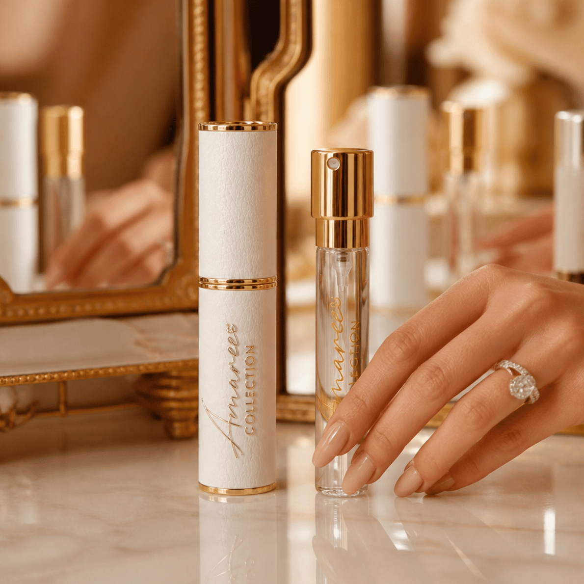 A hand with manicured nails and a ring holds a clear glass perfume rollerball next to a white cylindrical bottle with gold trim and a gold cap. The white bottle features the script logo 'Anmaree COLLECTION'.