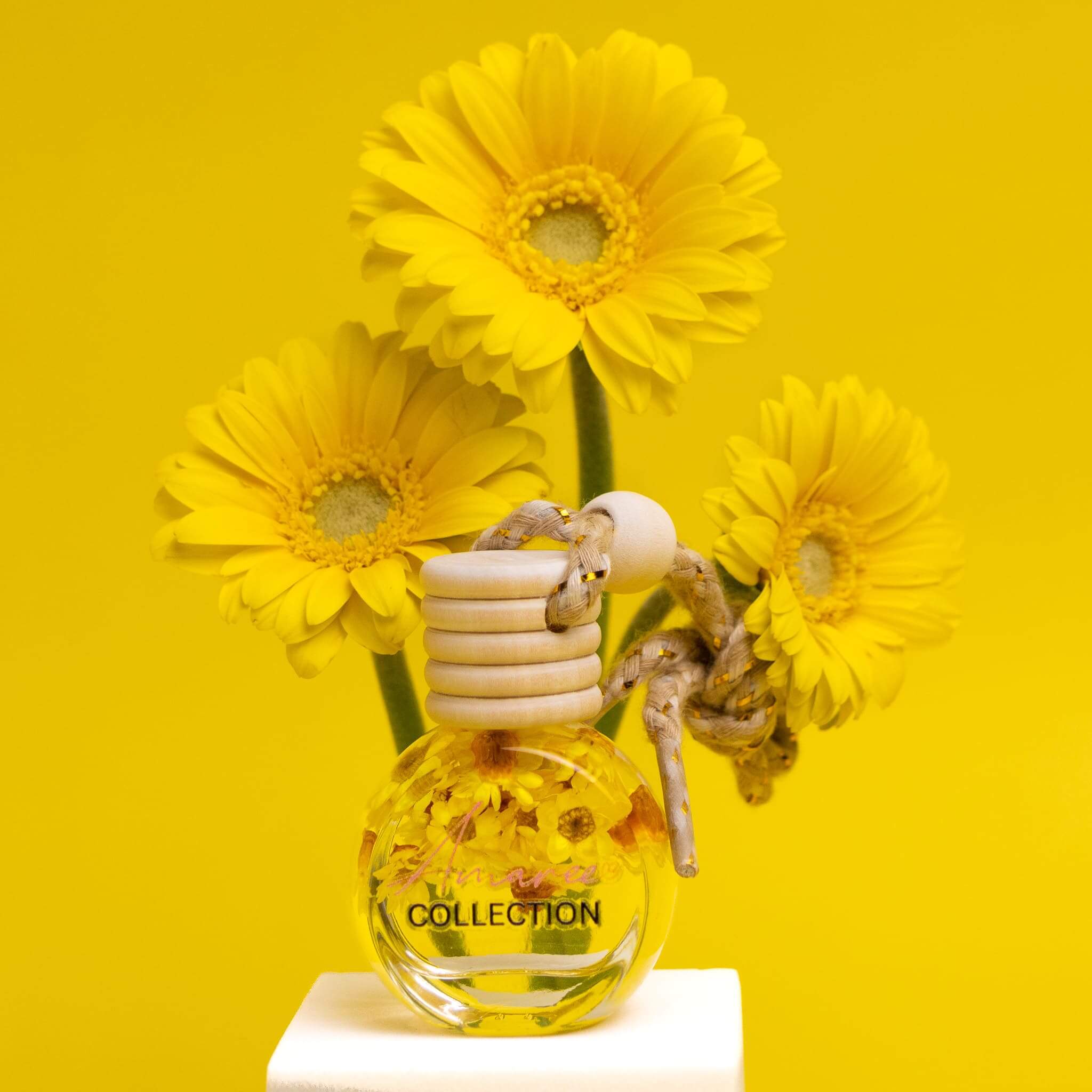Vanilla, Patchouli & Sandalwood Car Diffuser product bottle with yellow flowers on bright yellow background