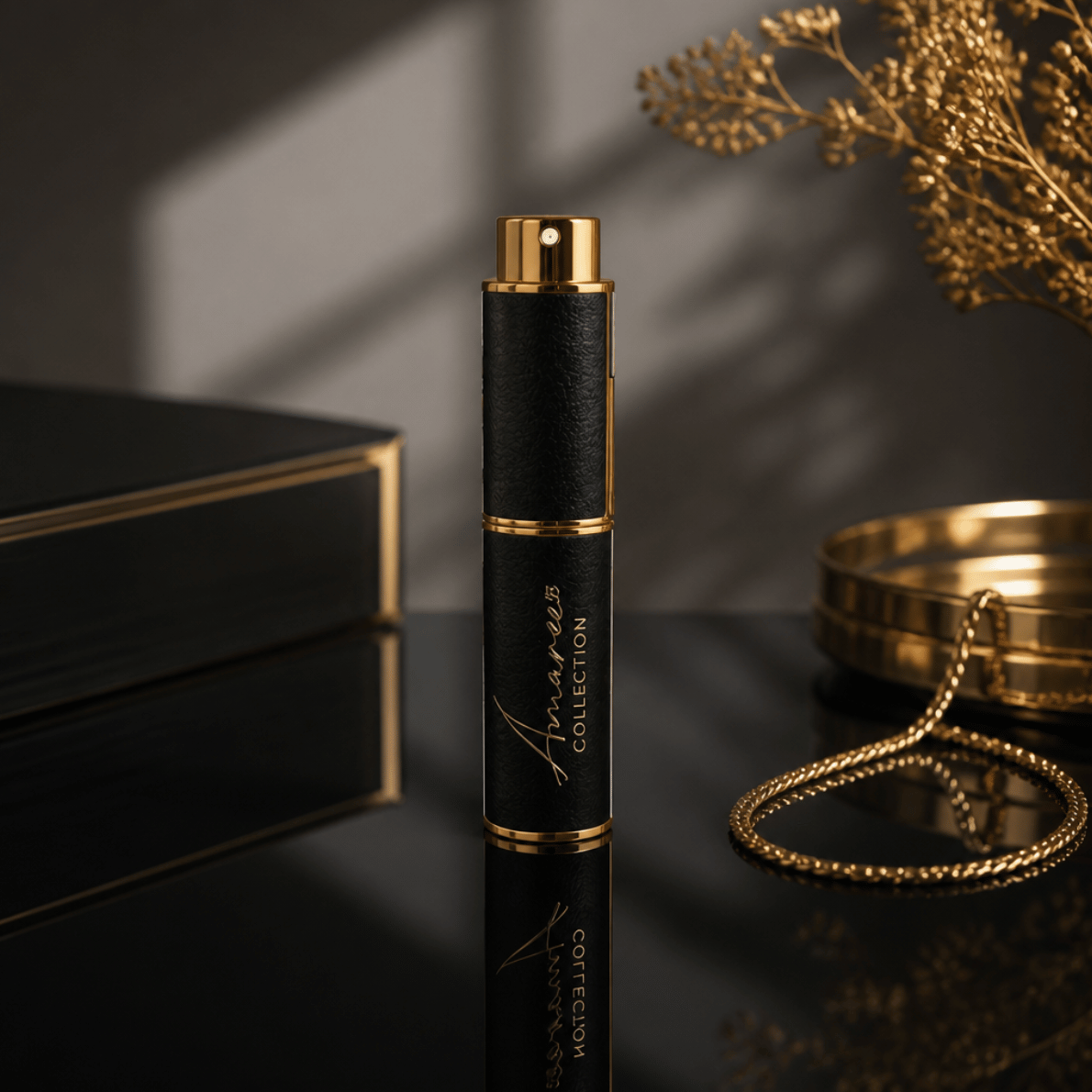 A sleek black cylindrical perfume bottle with gold trim and a gold cap stands on a glossy black surface. The bottle is branded &