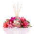 Aromatherapy diffuser with wooden sticks surrounded by pink flowers on a white background