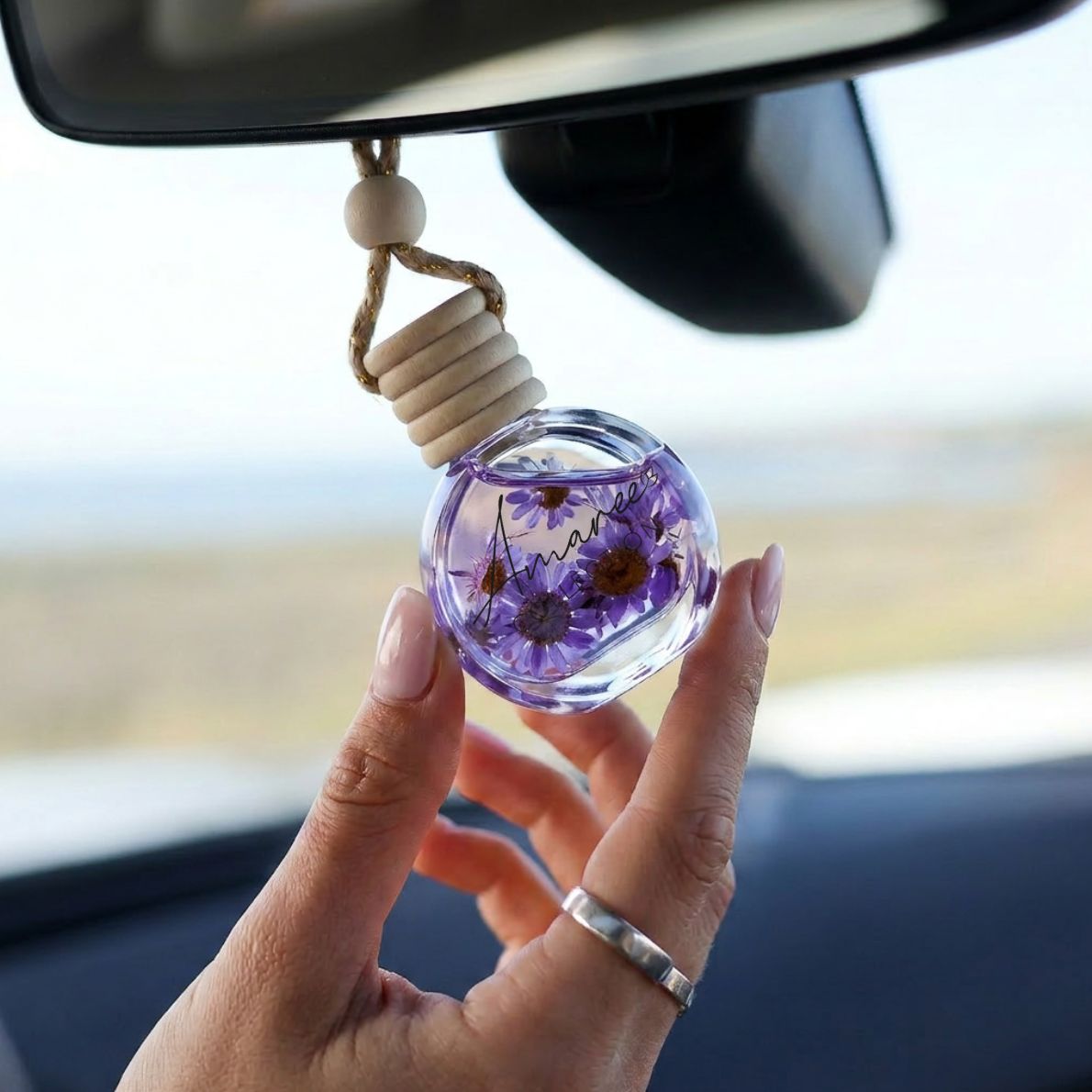 Hand holding a car air freshener with dried flowers inside, hanging from a car&