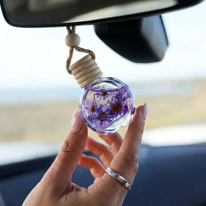 Hand holding a car air freshener with dried flowers inside, hanging from a car&