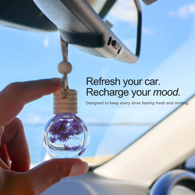 A hand holds a clear glass car air freshener bottle with dried purple flowers inside, shown hanging near a rearview mirror in a car with blue sky visible outside. Text on the image reads: &
