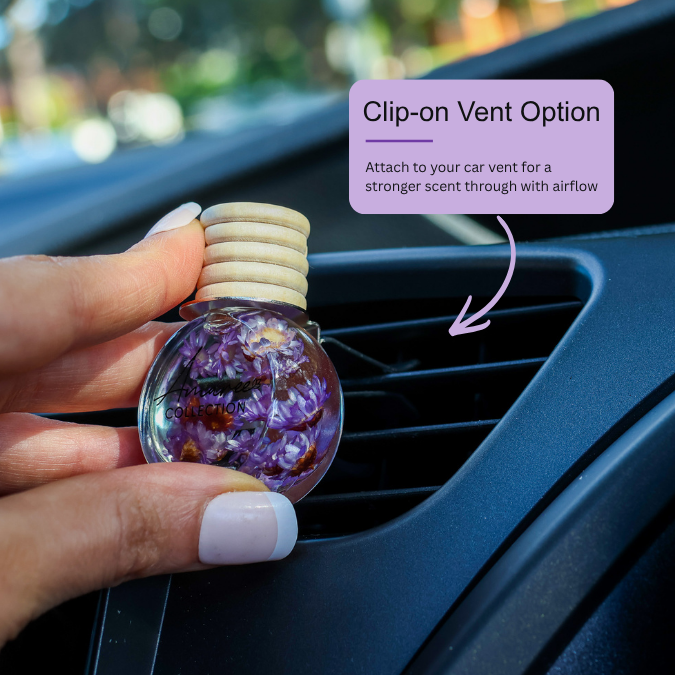 A hand holds a clear round car air freshener or clip-on vent diffuser with dried purple flowers inside, positioned near a car vent. A purple text box says &