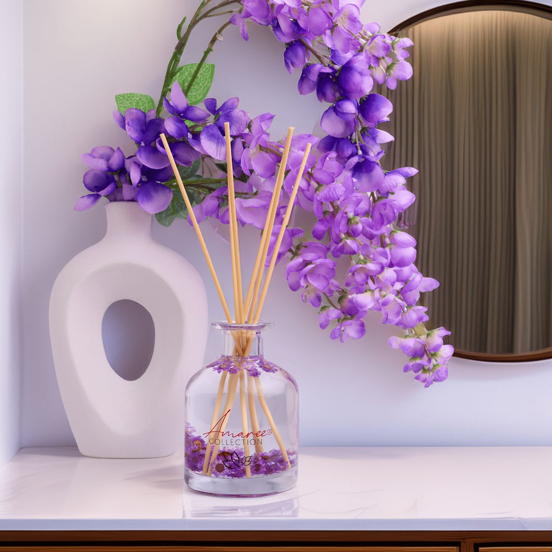 Decorative diffuser with purple flowers and sticks on a white surface, with a mirror and white vase in the background.