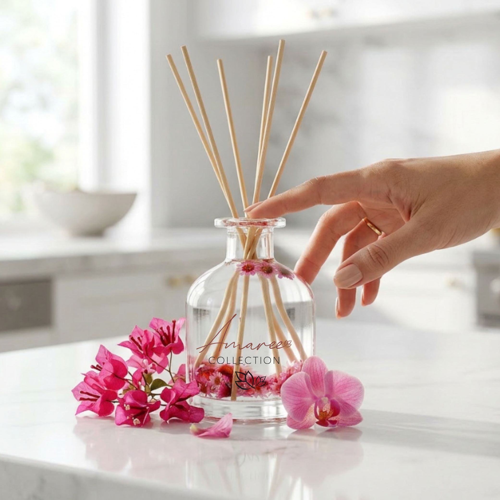 Hand holding a long lasting reed diffuser with pink flowers on a white surface