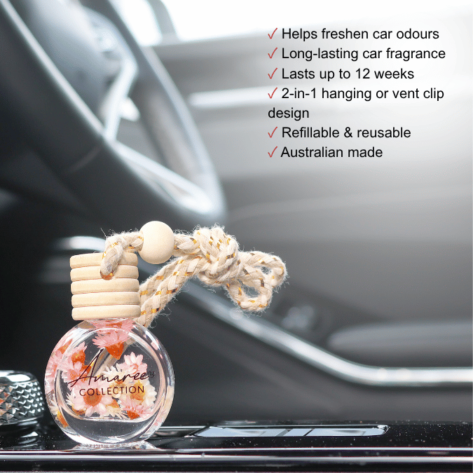 A round clear glass car air freshener bottle with dried flowers inside, topped with stacked light wood discs and a knotted beige cord, placed on a car dashboard. Black text on the right lists benefits such as freshening car odours and lasting up to 12 weeks.