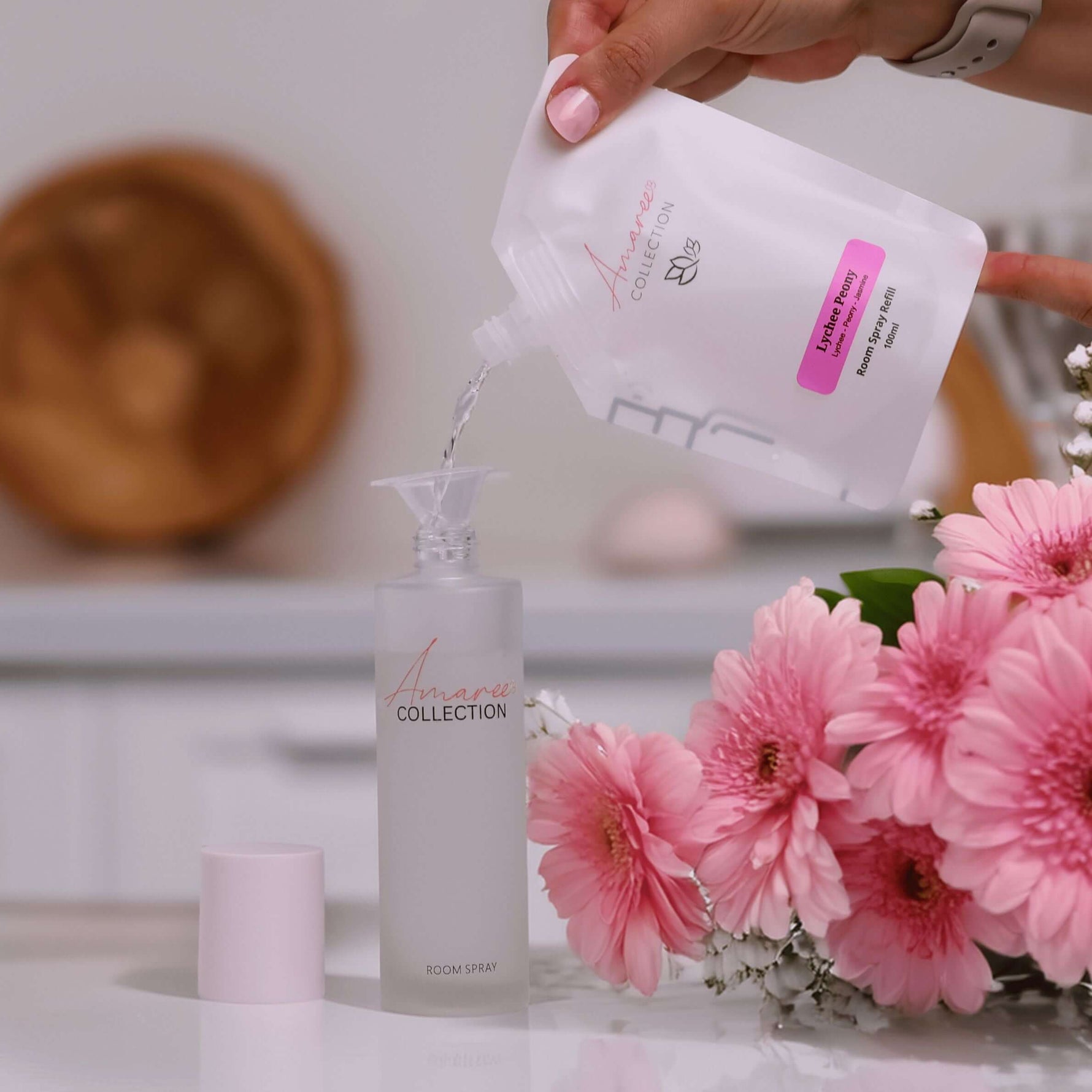 Pouring Lychee Peony Room Spray Refill 100ml into a stylish bottle with blooming pink flowers.