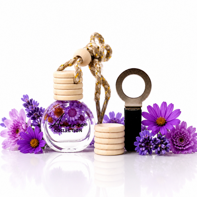 A glass diffuser bottle with purple flowers inside, a wooden stopper, a braided hanging cord, and a black ring-shaped accessory, styled with purple flowers on a white reflective surface.
