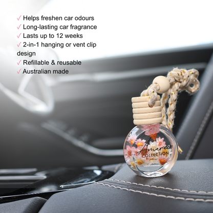A clear glass car fragrance bottle with dried flowers and a knotted rope hanger sits on a car seat, with marketing text overlaid on the left side. The bottle is labeled &