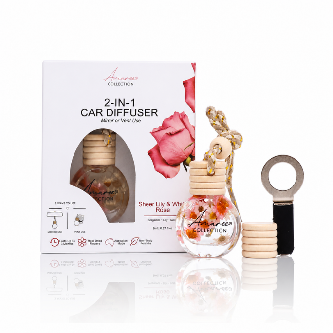 Anaroees Collection 2-in-1 Car Diffuser in Sheer Lily &amp; White Rose fragrance, shown with its retail packaging box, a clear glass bottle with a wooden cap, a gold-and-white hanging cord, and a black-and-gold key-shaped diffuser accessory on a white reflective background.