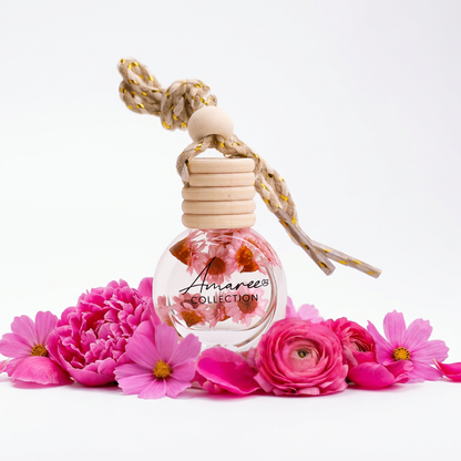 Small clear bottle with wooden cap and floral design, surrounded by pink flowers on a white background