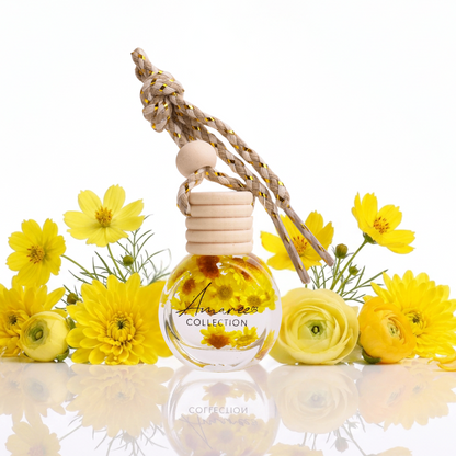 Car air freshener with wooden holder and clear bottle surrounded by yellow flowers on a reflective surface.