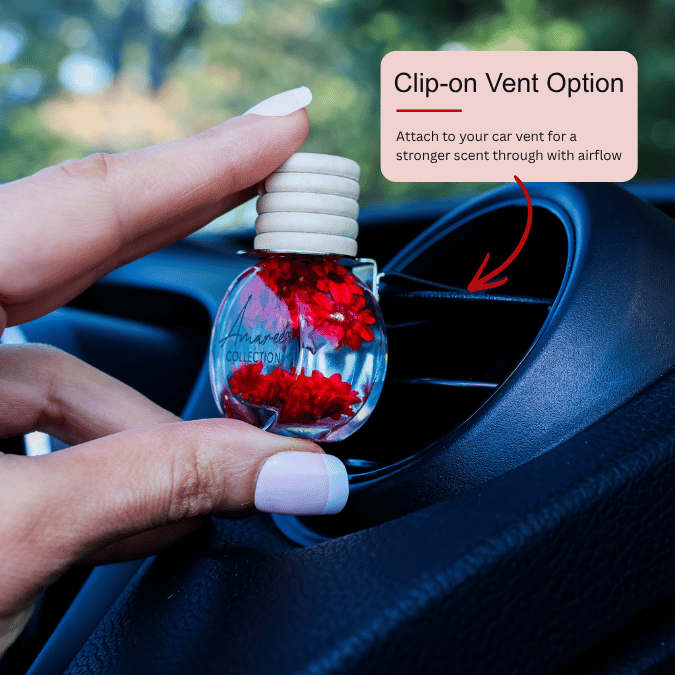 A hand holds a small clear car air freshener bottle with red flower pieces inside, positioned over a car air vent. A text box says &