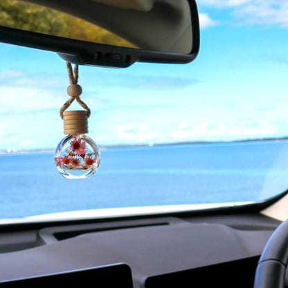 Car interior with a decorative hanging item featuring flowers, overlooking a scenic ocean view.