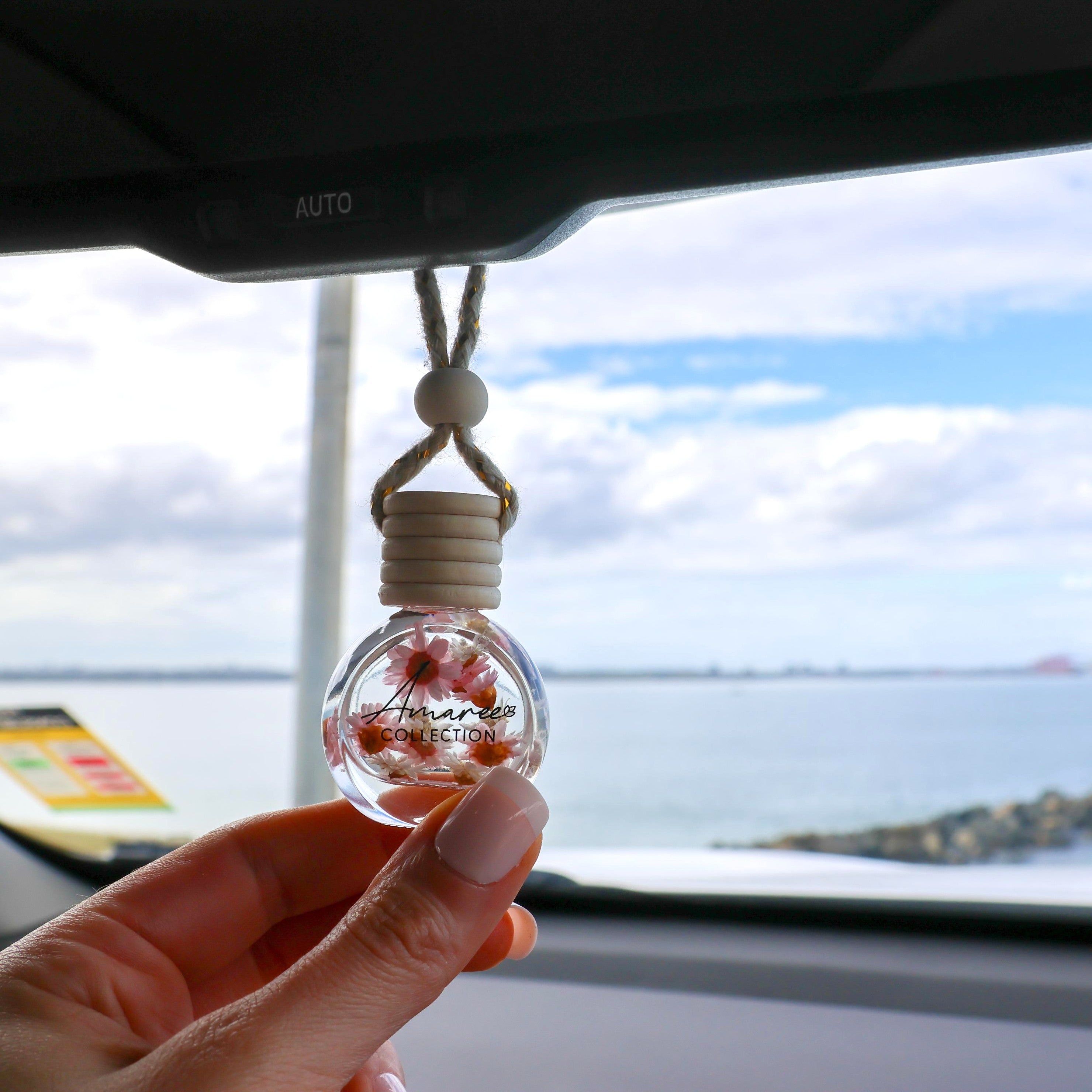 Car air freshener with floral design held by a hand, car interior and window background