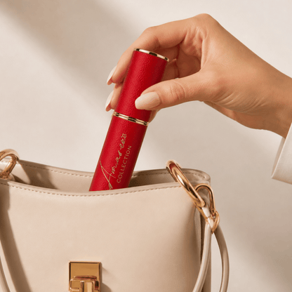 A hand with manicured nails holds a red lipstick tube with gold trim, inserting it into a beige handbag with gold hardware.
