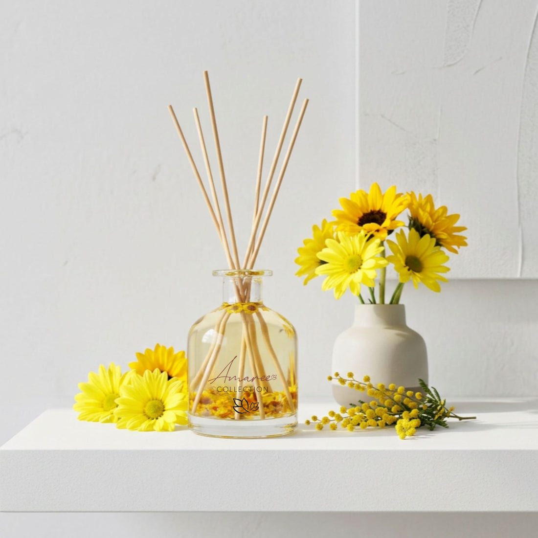 A diffuser with reeds and a small vase of yellow flowers on a white surface.