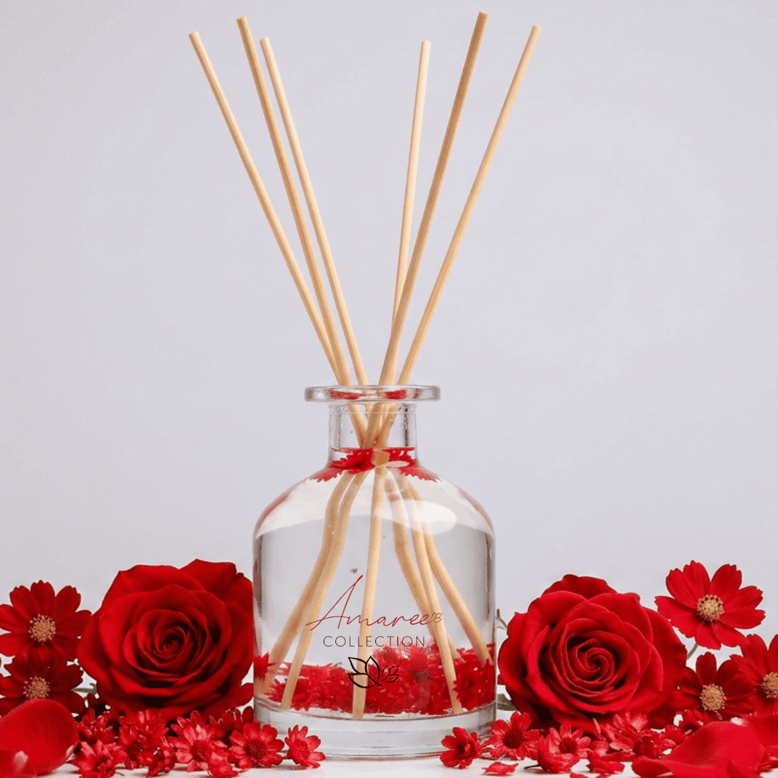 Aromatherapy diffuser with wooden sticks surrounded by red flowers on a light gray background