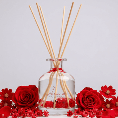 Aromatherapy diffuser with wooden sticks surrounded by red flowers on a light gray background