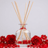 Aromatherapy diffuser with wooden sticks surrounded by red flowers on a light gray background