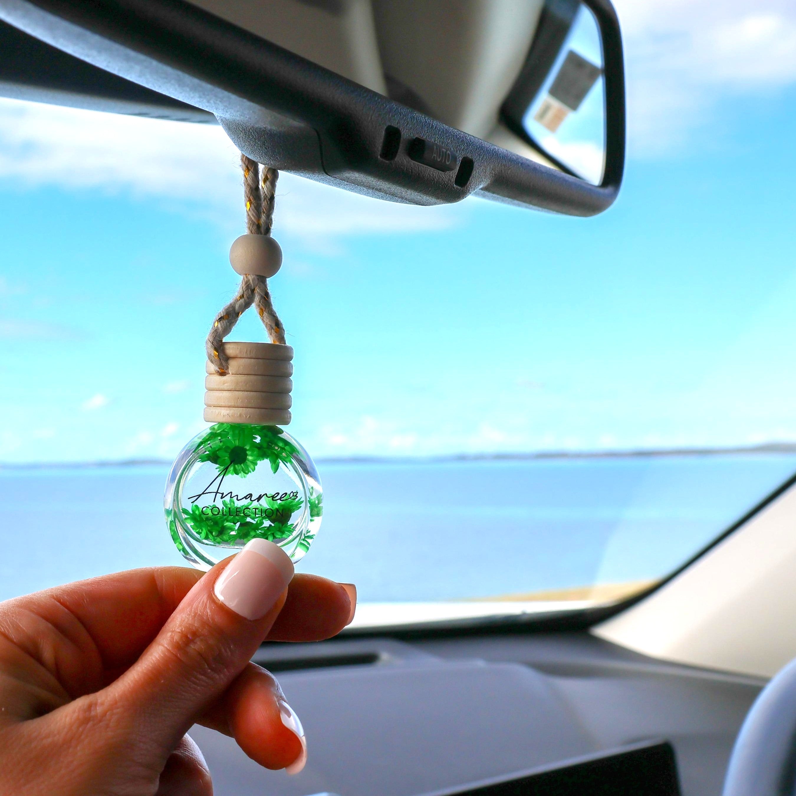 Car hanging ornament with green decorative item held by a hand inside a car.