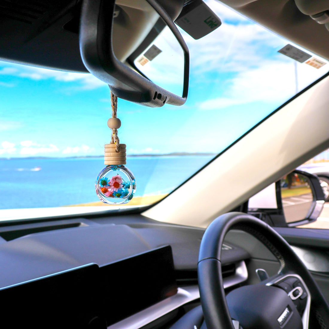 Car interior with a decorative hanging ornament near the rearview mirror, overlooking a scenic view.