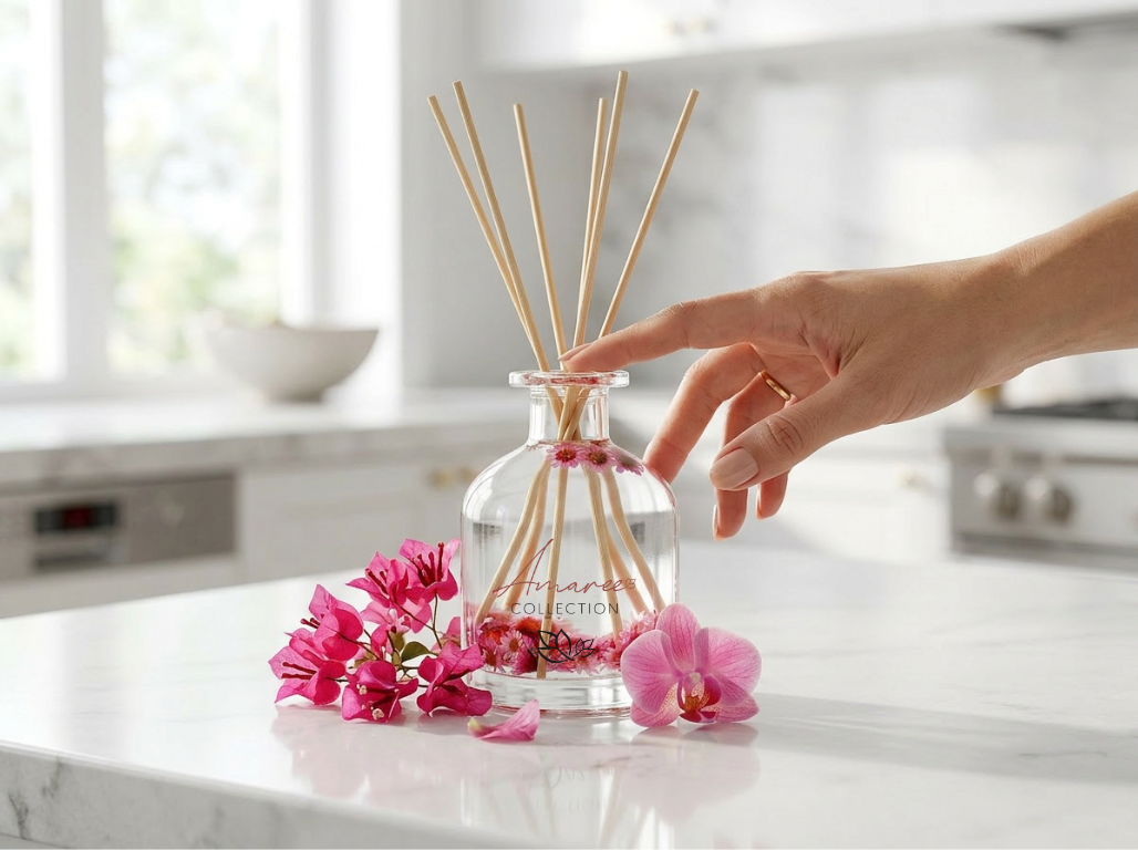 Hand reaching for a diffuser with reeds and pink flowers on a marble surface