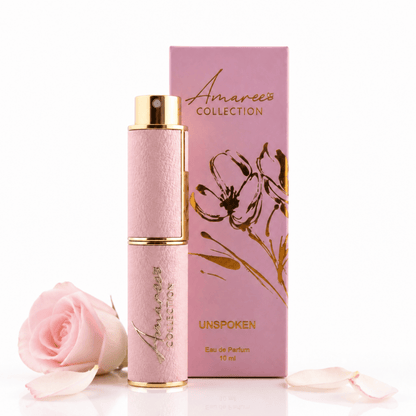 A pink perfume bottle with gold trim stands in front of its matching pink box, both printed with the Amaree Collection logo and floral artwork. A pale pink rose and a few loose petals are placed at the base on a clean white background.