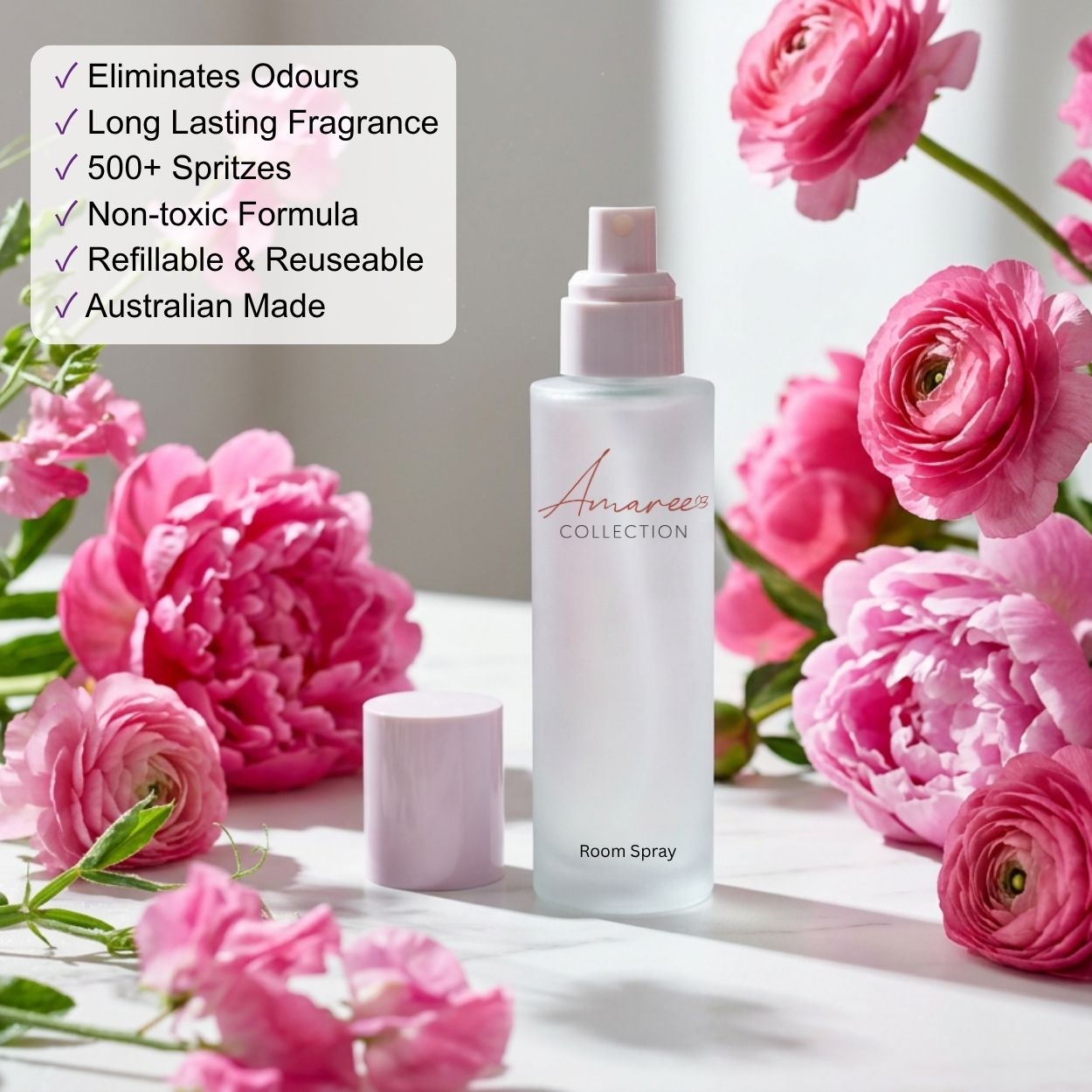 A frosted glass room spray bottle with a pale pink cap stands on a white surface surrounded by pink flowers. A white text box on the left lists product benefits in bullet points, including &