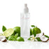 A frosted glass room spray bottle from Amaree Collection, surrounded by fresh green limes, basil leaves, white flowers, and coconut halves on a reflective white surface.